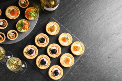 Delicious canapes and glasses of white wine on black textured table, flat lay. Space for text