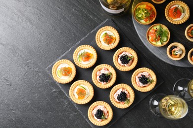 Photo of Delicious canapes and glasses of white wine on black textured table, flat lay. Space for text