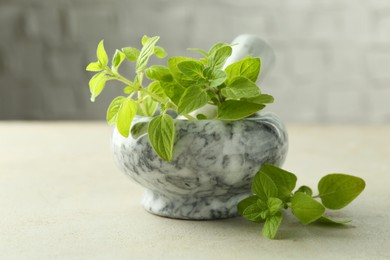 Photo of Fresh green oregano in mortar and pestle on light textured table, closeup