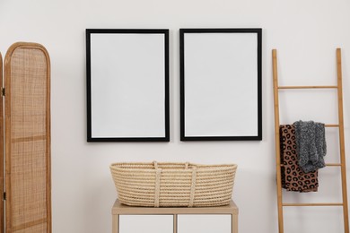 Empty frames hanging on wall, wicker basket and wooden ladder in room