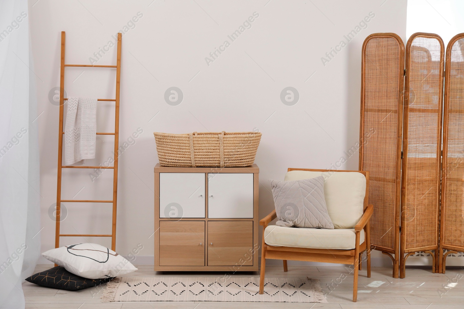 Photo of Armchair with cushion, wicker basket on nightstand and wooden ladder in room