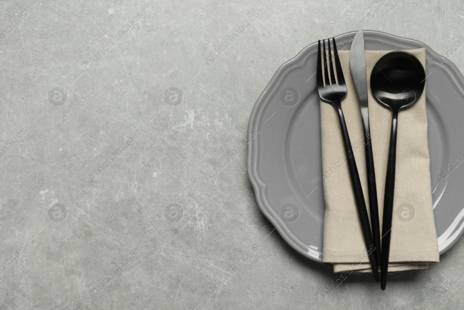 Photo of Stylish cutlery, napkin and plate on grey table, top view. Space for text