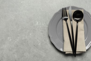 Stylish cutlery, napkin and plate on grey table, top view. Space for text