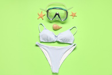 Photo of Striped swimsuit, diving mask, seashell and starfishes on green background, flat lay