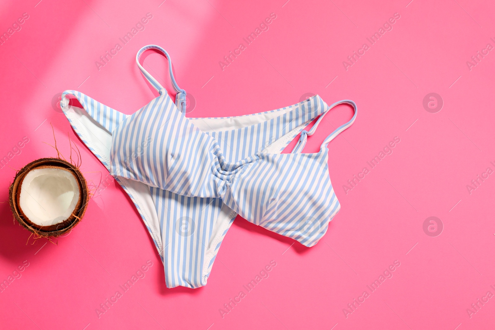 Photo of Striped swimsuit and coconut on pink background, flat lay. Space for text