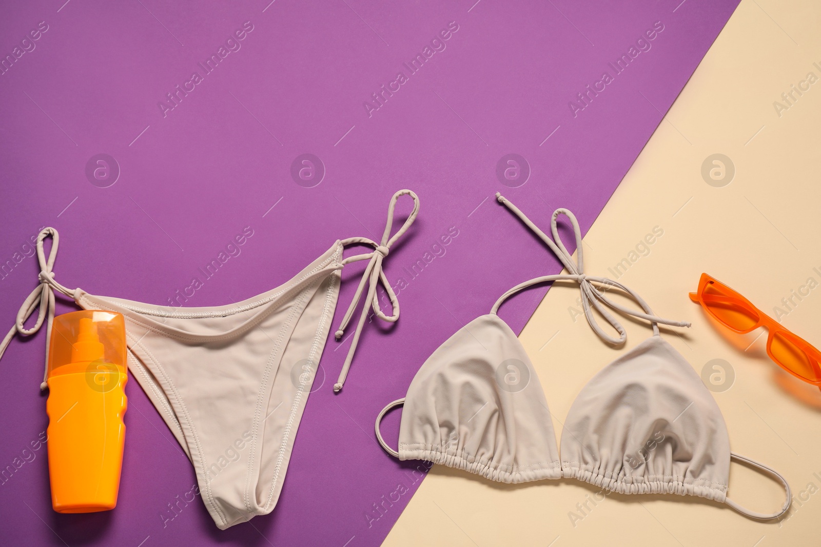 Photo of Beige swimsuit, sunglasses and sunscreen on color background, flat lay. Space for text