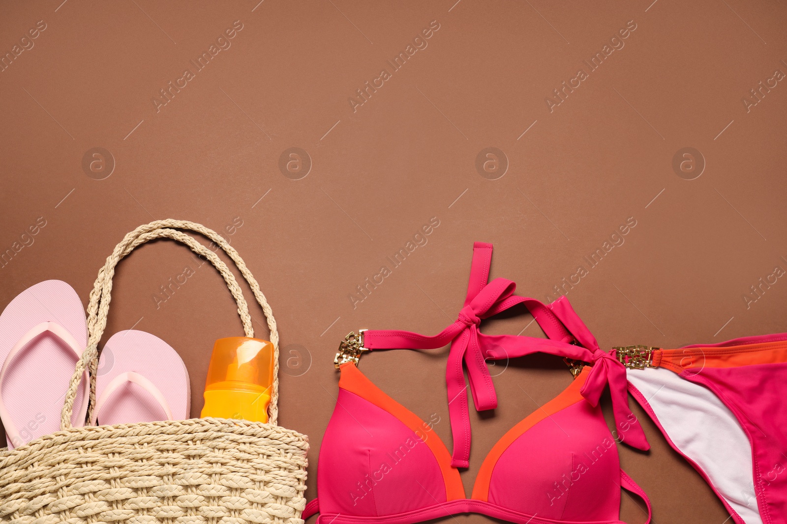 Photo of Red swimsuit, bag, sunscreen and flip flops on brown background, flat lay. Space for text