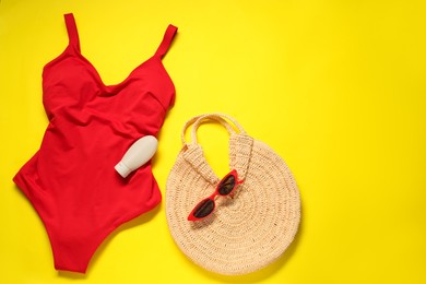 Photo of Red swimsuit, bag, sunglasses and sunscreen on yellow background, flat lay. Space for text