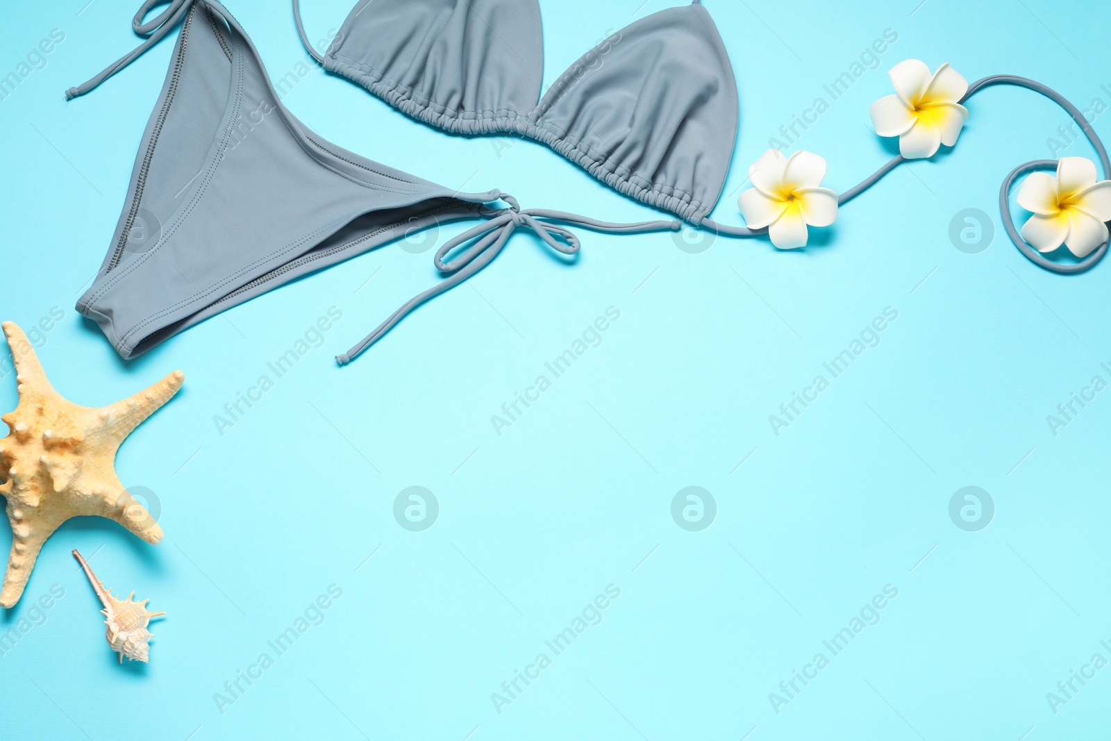 Photo of Flat lay composition with beautiful swimsuit, flowers and starfish on light blue background. Space for text