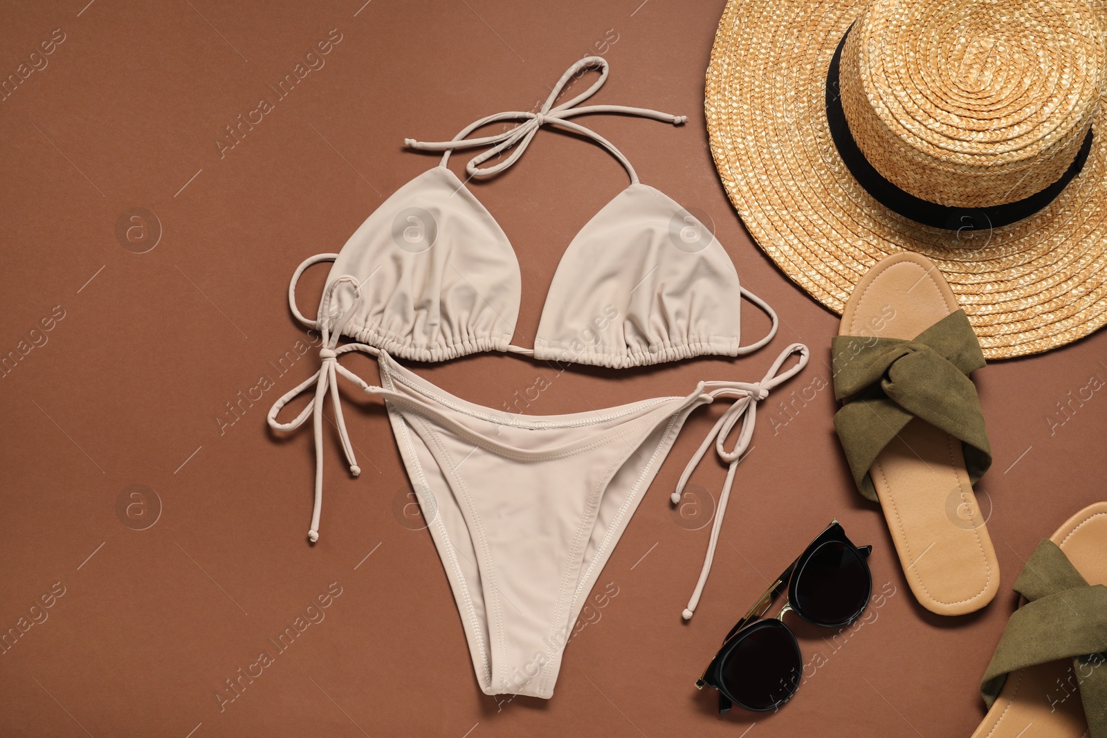 Photo of Flat lay composition with beige swimsuit, hat and slippers on brown background