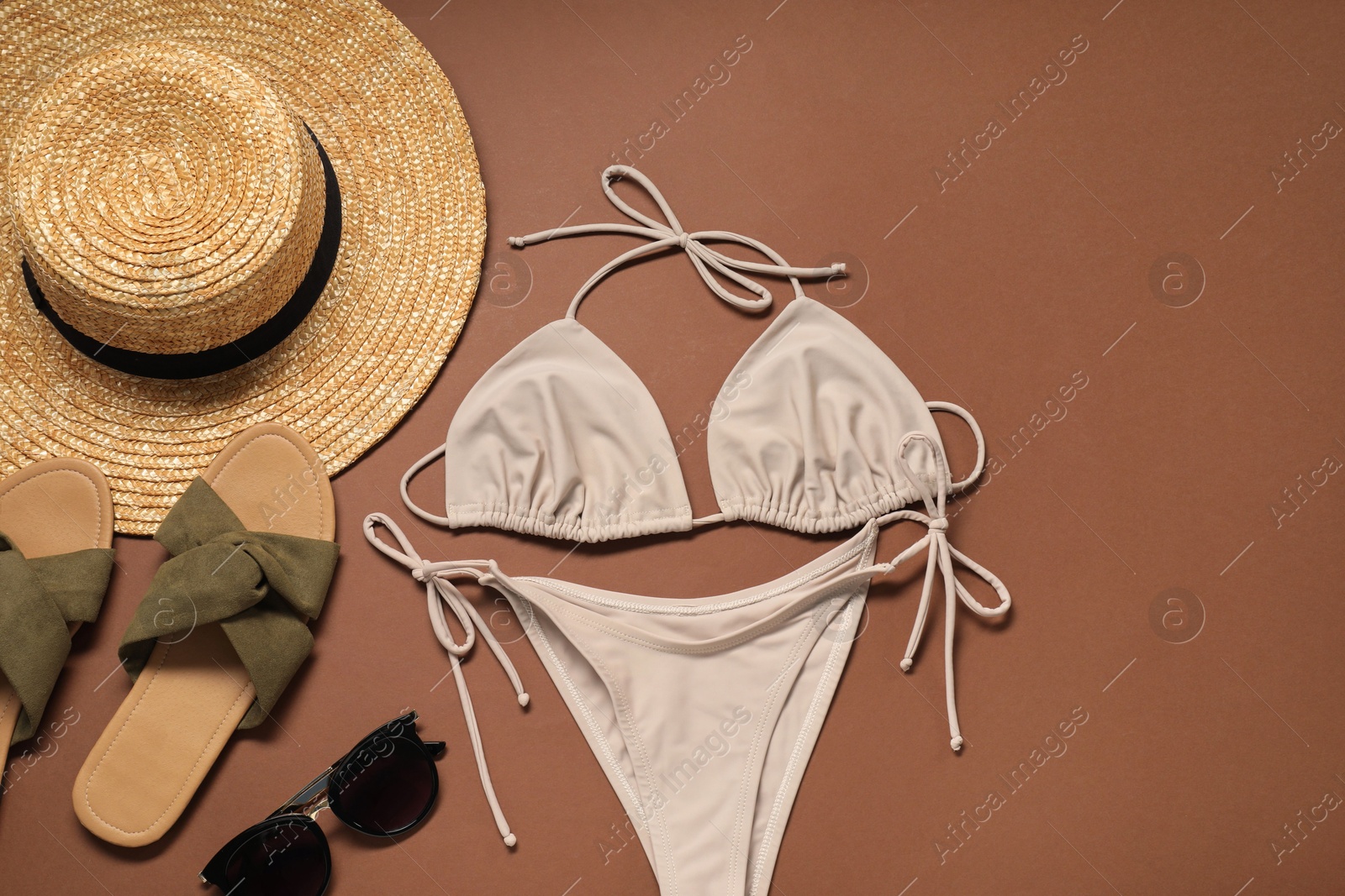 Photo of Flat lay composition with beige swimsuit, hat and slippers on brown background. Space for text