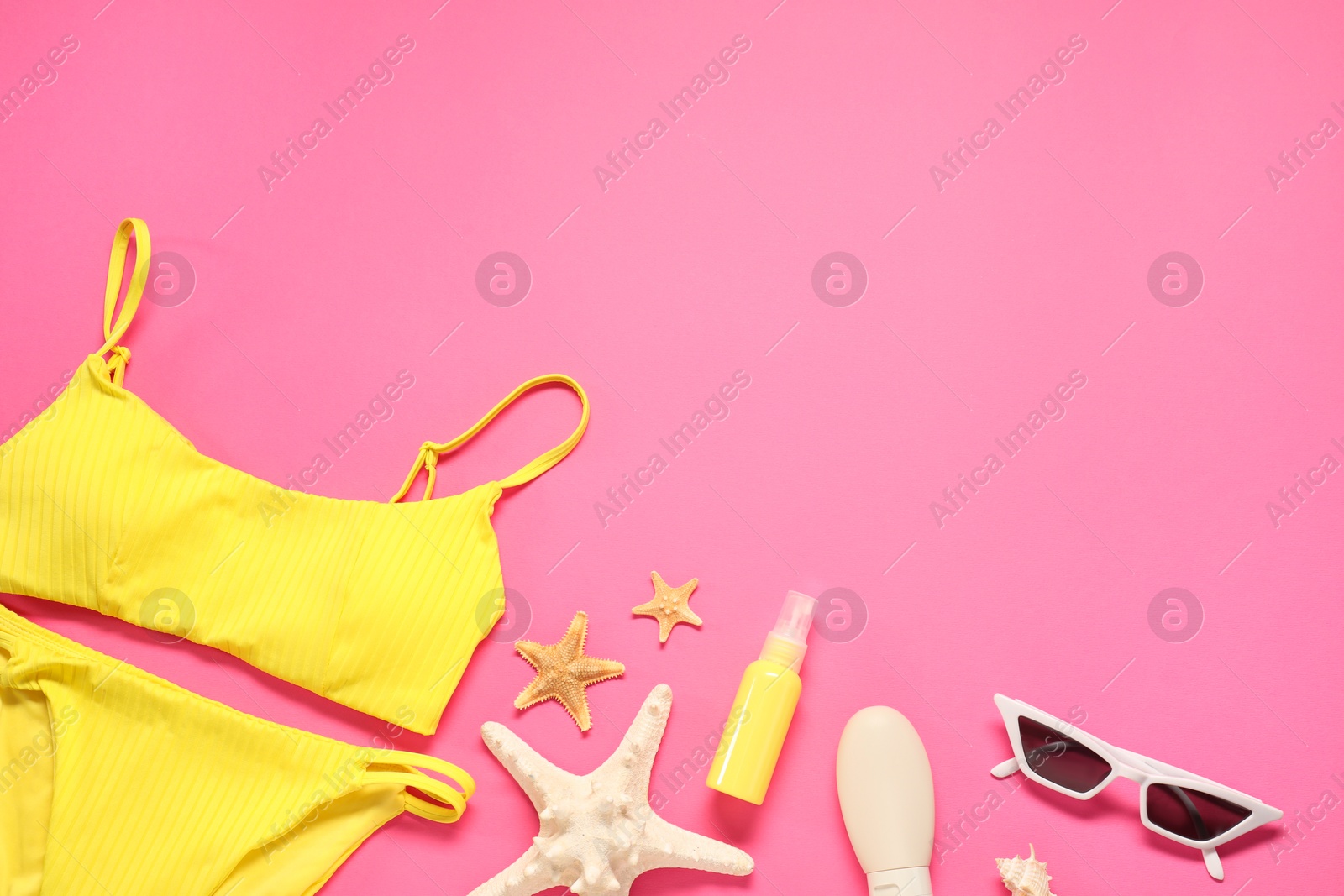 Photo of Flat lay composition with yellow swimsuit, sunscreen and sunglasses on pink background. Space for text