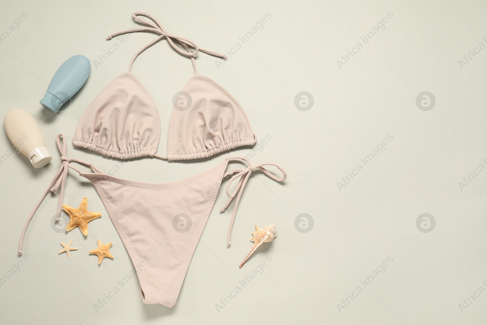 Photo of Beautiful swimsuit, sunscreens and starfishes on beige background, flat lay. Space for text