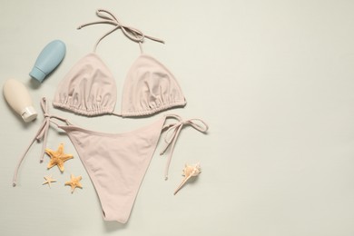 Beautiful swimsuit, sunscreens and starfishes on beige background, flat lay. Space for text