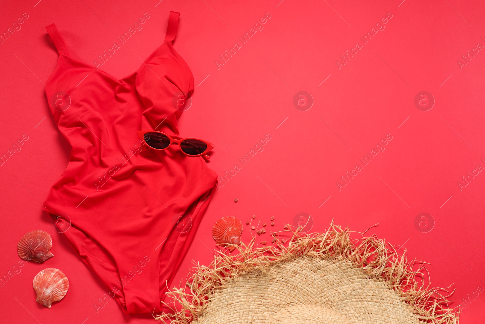 Photo of Beautiful swimsuit, sunglasses and seashells on red background, flat lay. Space for text