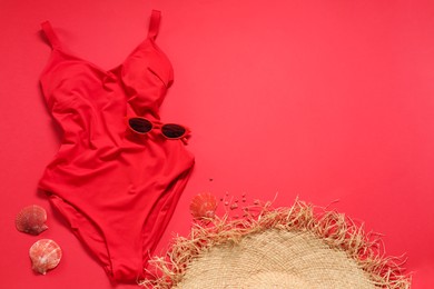 Photo of Beautiful swimsuit, sunglasses and seashells on red background, flat lay. Space for text