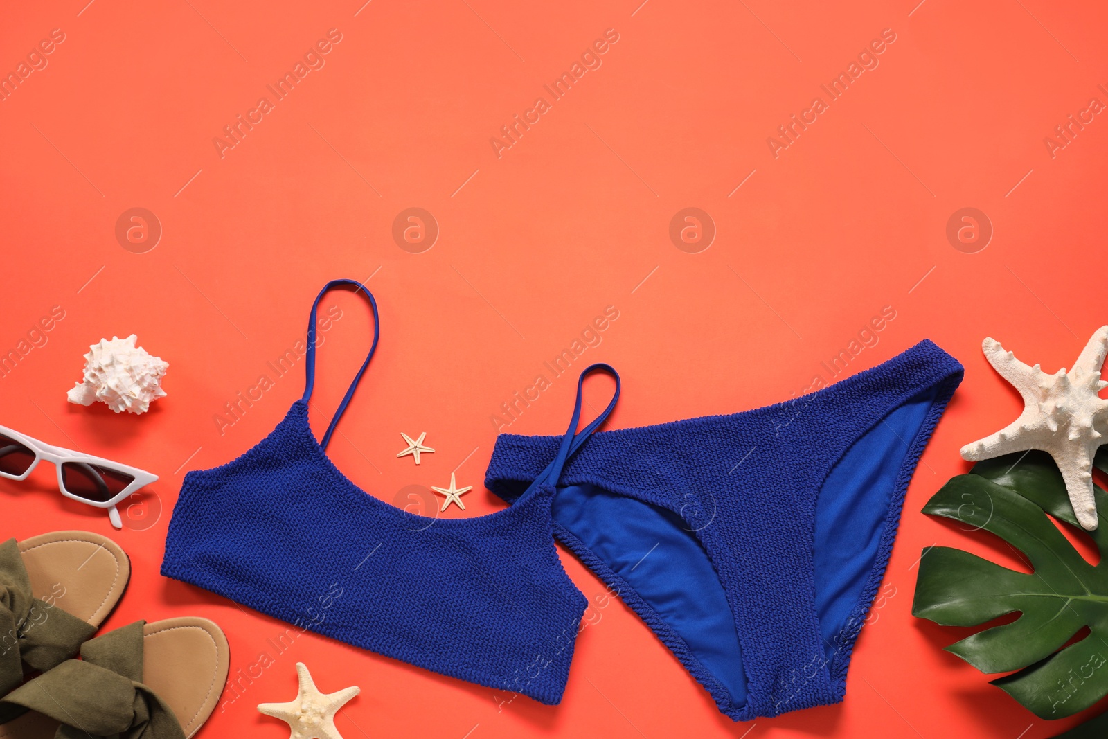 Photo of Flat lay composition with blue swimsuit and sunglasses on coral background. Space for text