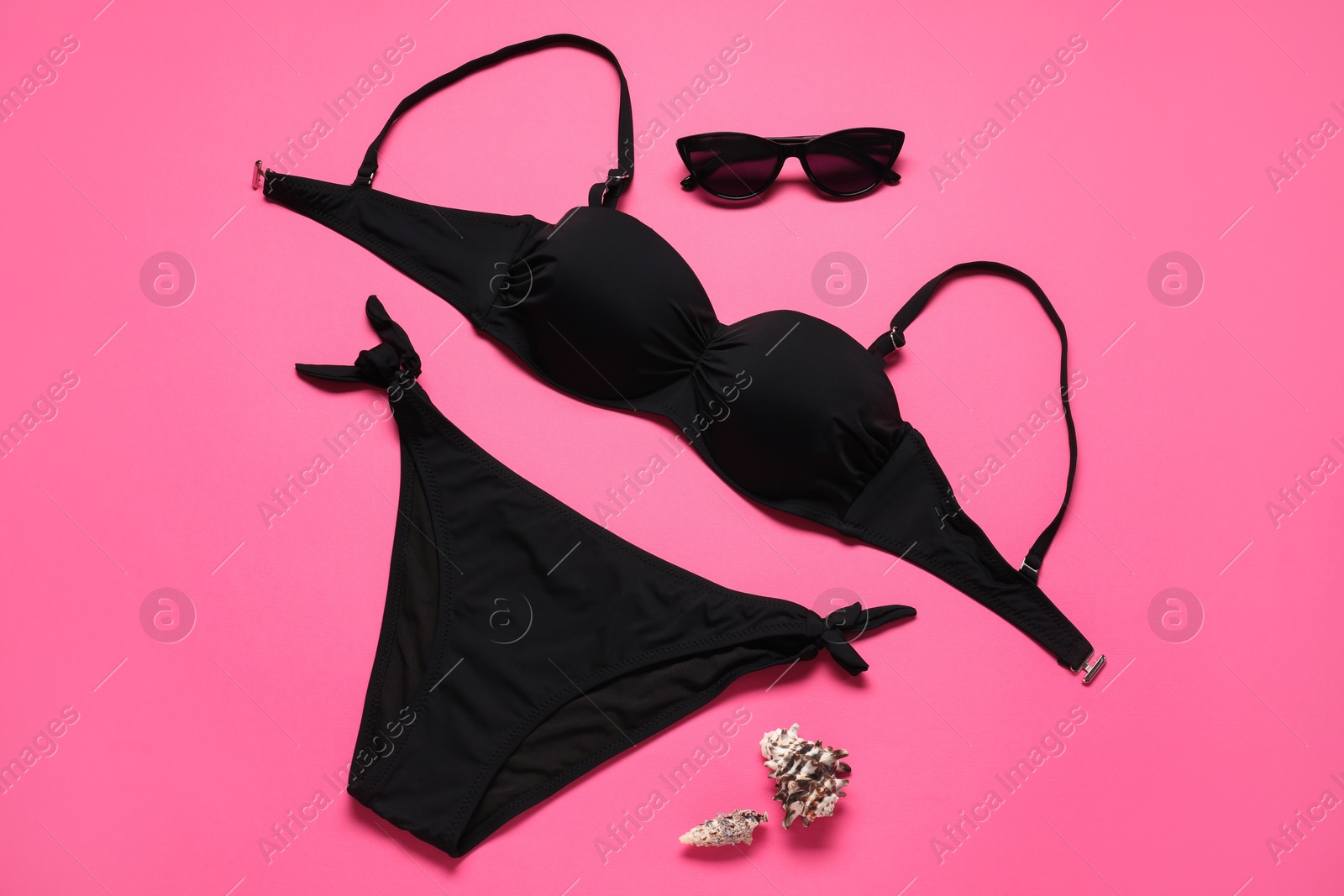 Photo of Black swimsuit, sunglasses and seashells on pink background, flat lay