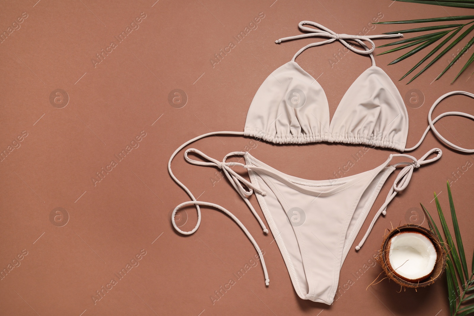 Photo of Beautiful swimsuit, coconut and palm leaves on brown background, flat lay. Space for text