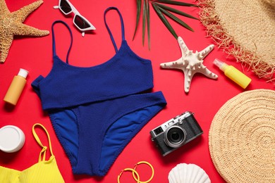 Flat lay composition with blue swimsuit, camera and bag on red background