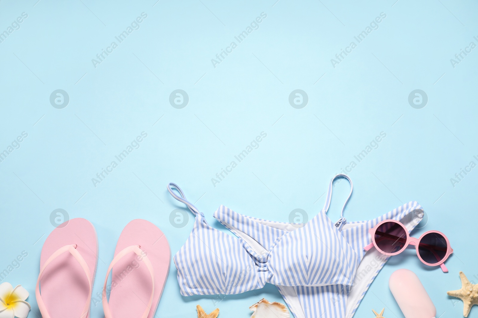 Photo of Flat lay composition with striped swimsuit and sunglasses on light blue background. Space for text