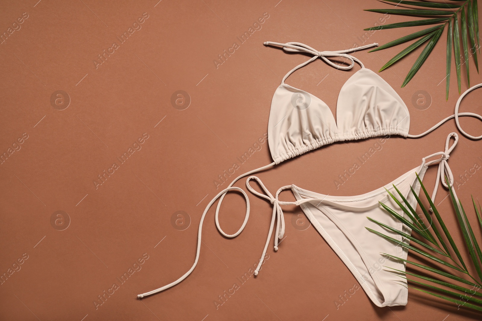 Photo of Beautiful swimsuit and palm leaves on brown background, flat lay. Space for text