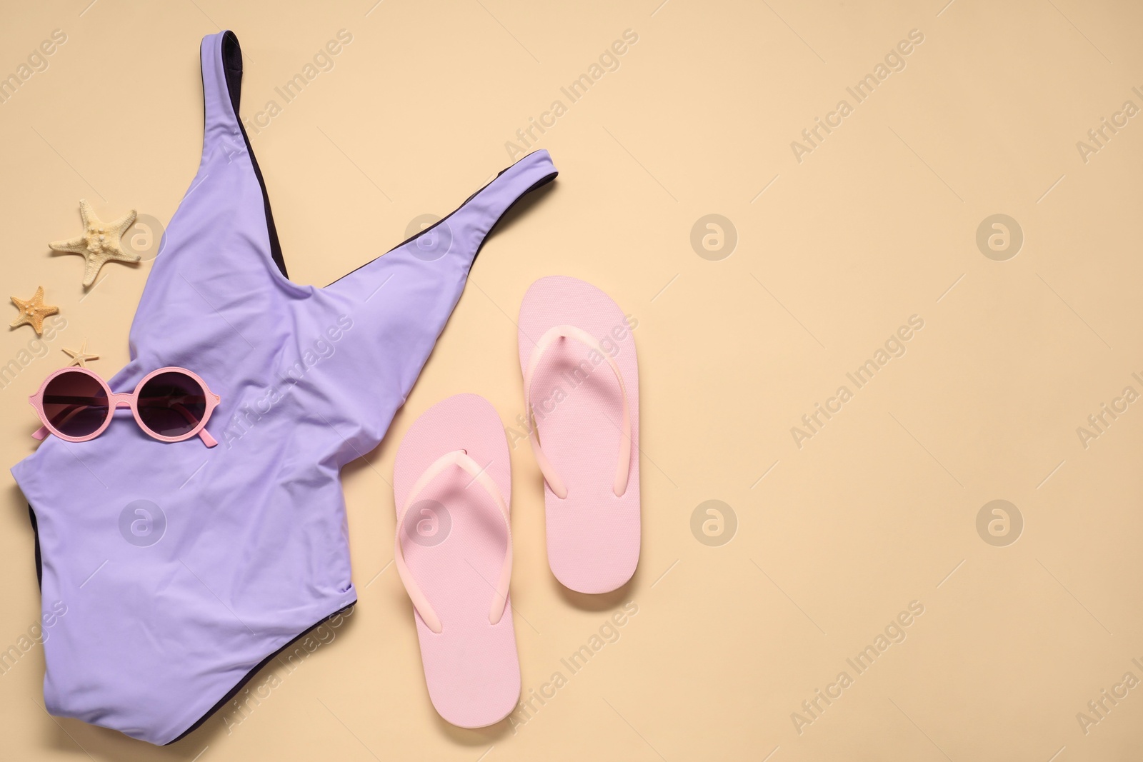 Photo of Violet swimsuit, sunglasses, starfishes and flip flops on beige background, flat lay. Space for text