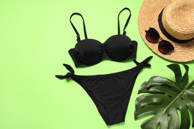 Flat lay composition with black swimsuit, sunglasses and hat on green background. Space for text