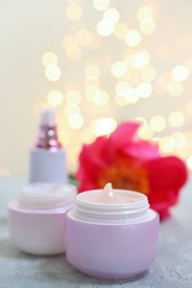 Set of different cosmetic products and peony flower on gray table against light background with blurred lights, closeup