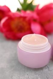 Photo of Jar of cream and peony flowers on gray table, closeup