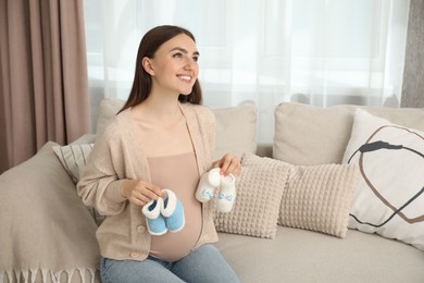 Photo of Expecting twins. Pregnant woman holding two pairs of shoes at home, space for text