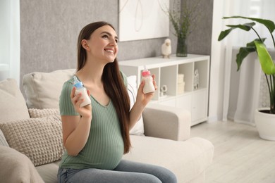 Photo of Expecting twins. Pregnant woman holding two bottles of milk at home, space for text