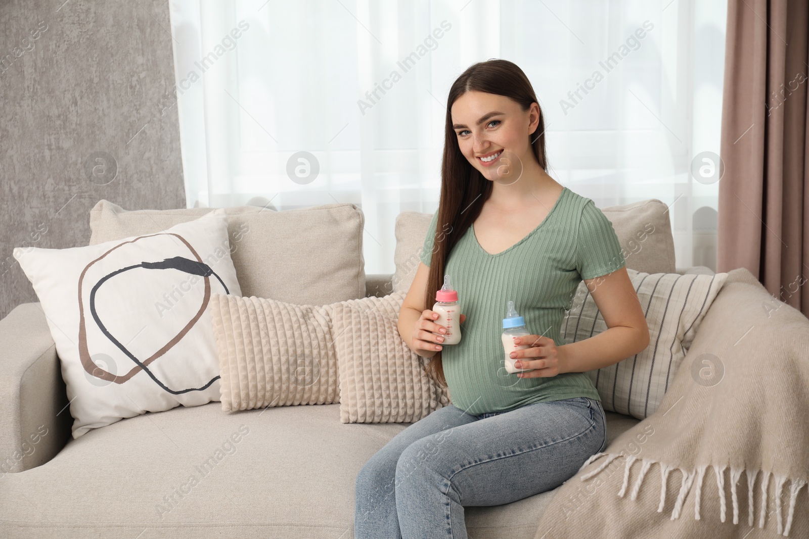 Photo of Expecting twins. Pregnant woman holding two bottles of milk at home, space for text