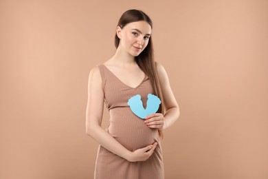 Photo of Expecting twins. Pregnant woman holding two paper cutouts of feet on light brown background