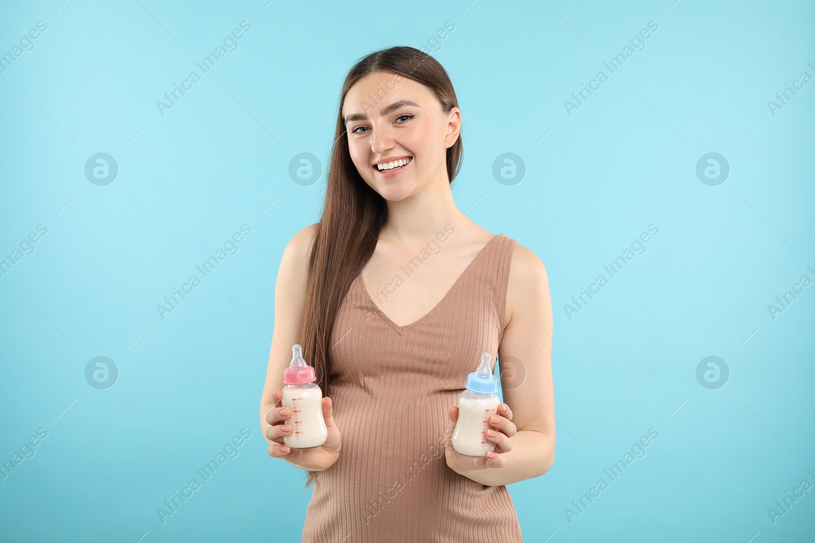 Photo of Expecting twins. Pregnant woman holding two bottles with milk on light blue background