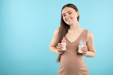 Photo of Expecting twins. Pregnant woman holding two bottles with milk on light blue background, space for text