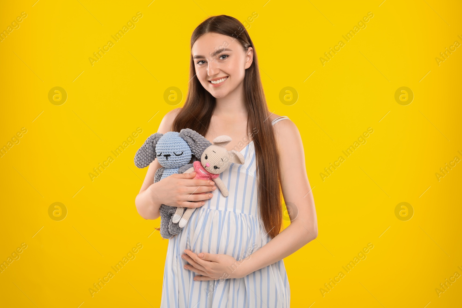 Photo of Expecting twins. Pregnant woman holding two toys on yellow background