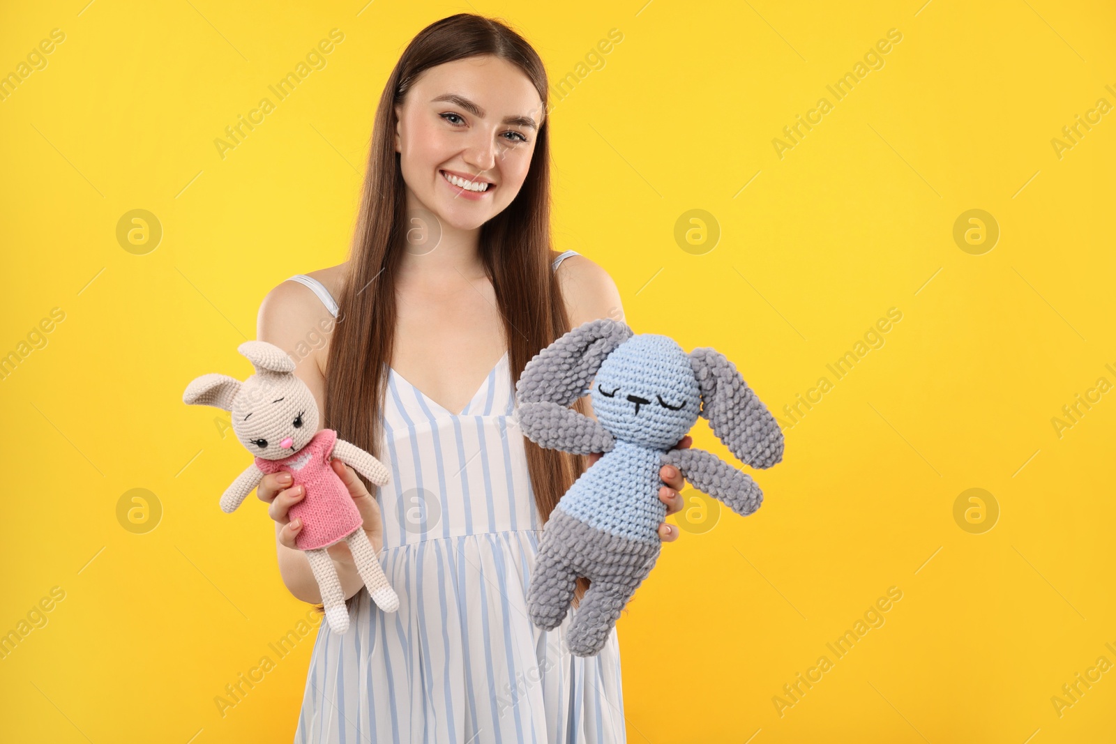 Photo of Expecting twins. Pregnant woman holding two toys on yellow background