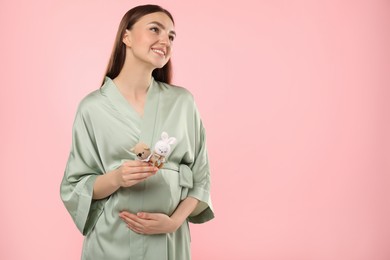 Photo of Expecting twins. Pregnant woman holding two toys on pink background, space for text