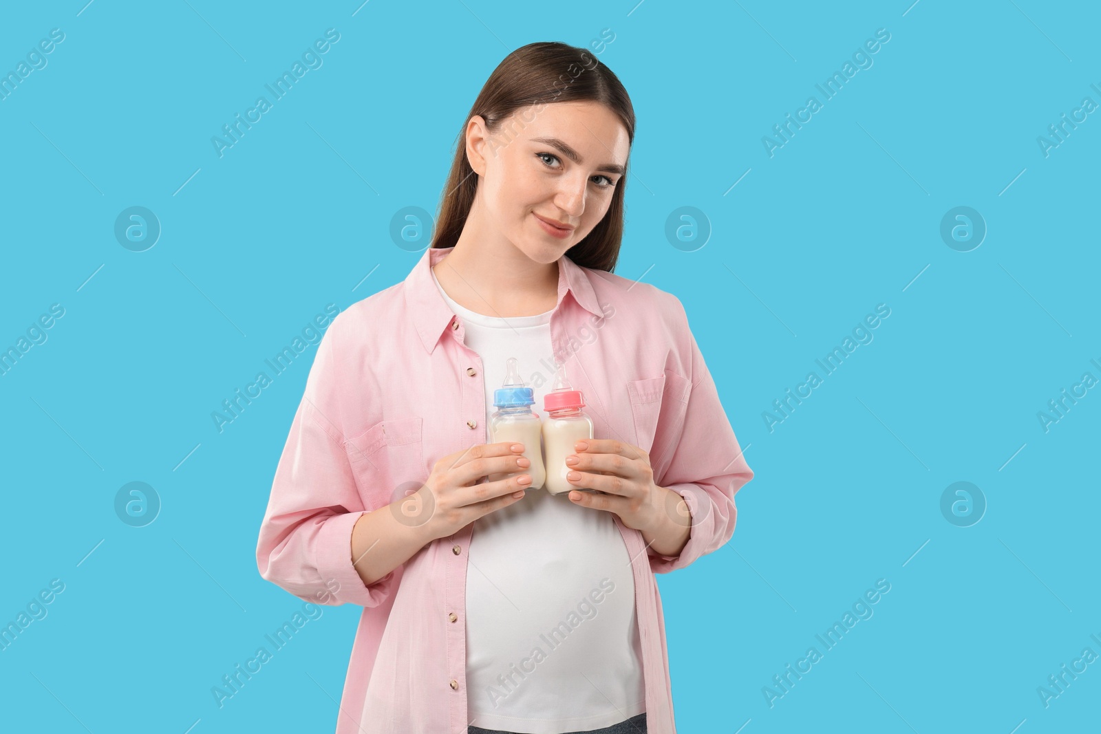 Photo of Expecting twins. Pregnant woman holding two bottles with milk on light blue background