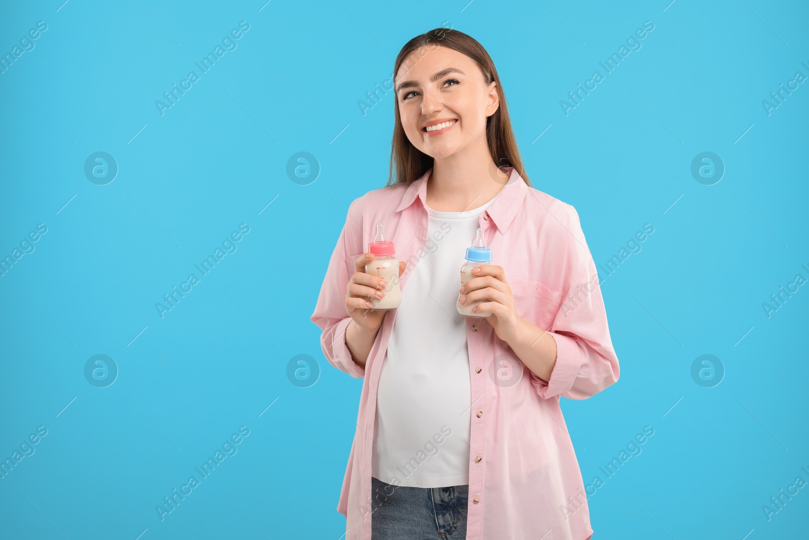 Photo of Expecting twins. Pregnant woman holding two bottles with milk on light blue background