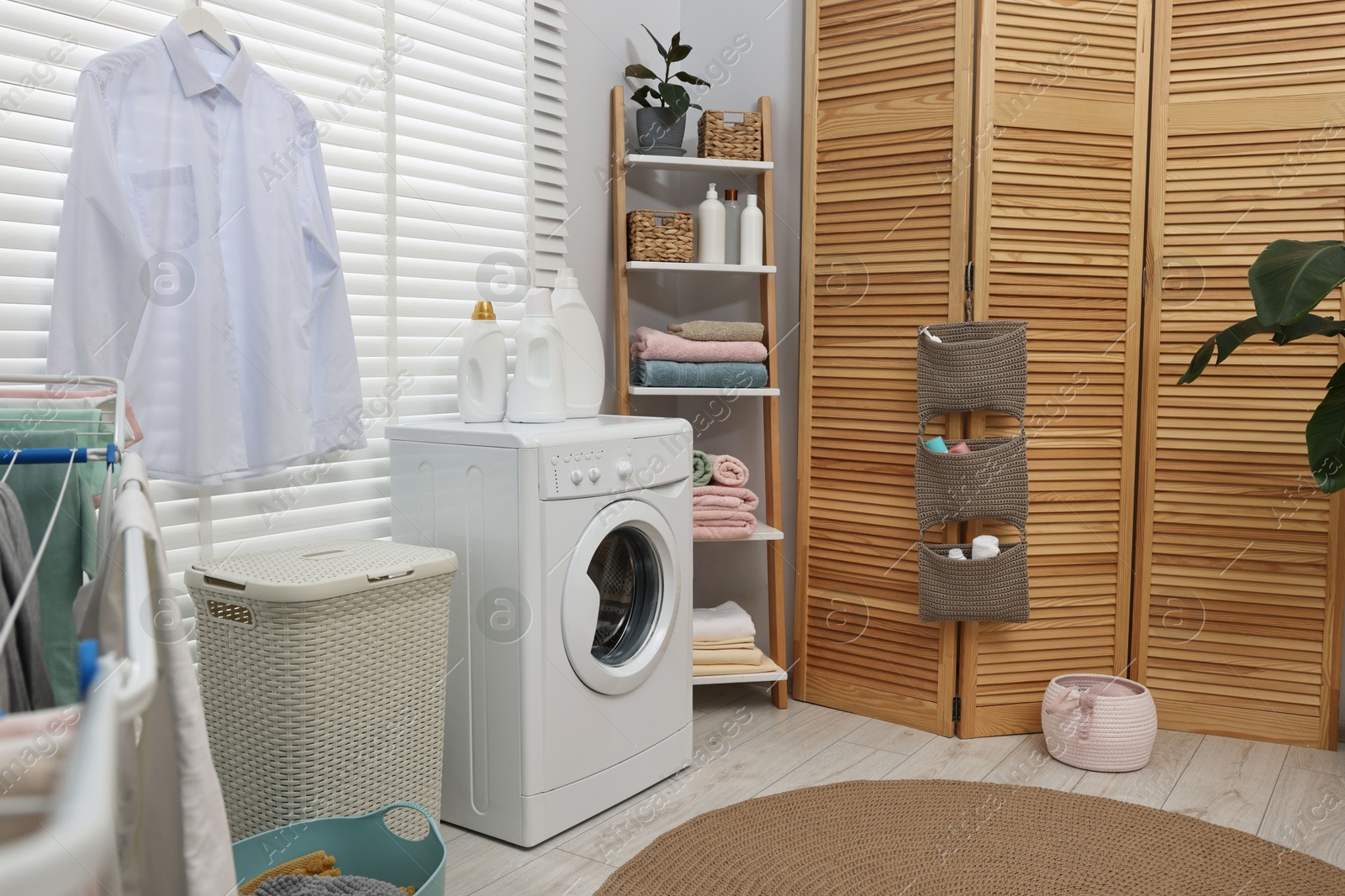 Photo of Washing machine, folding screen, detergents, towels and basket in laundry room