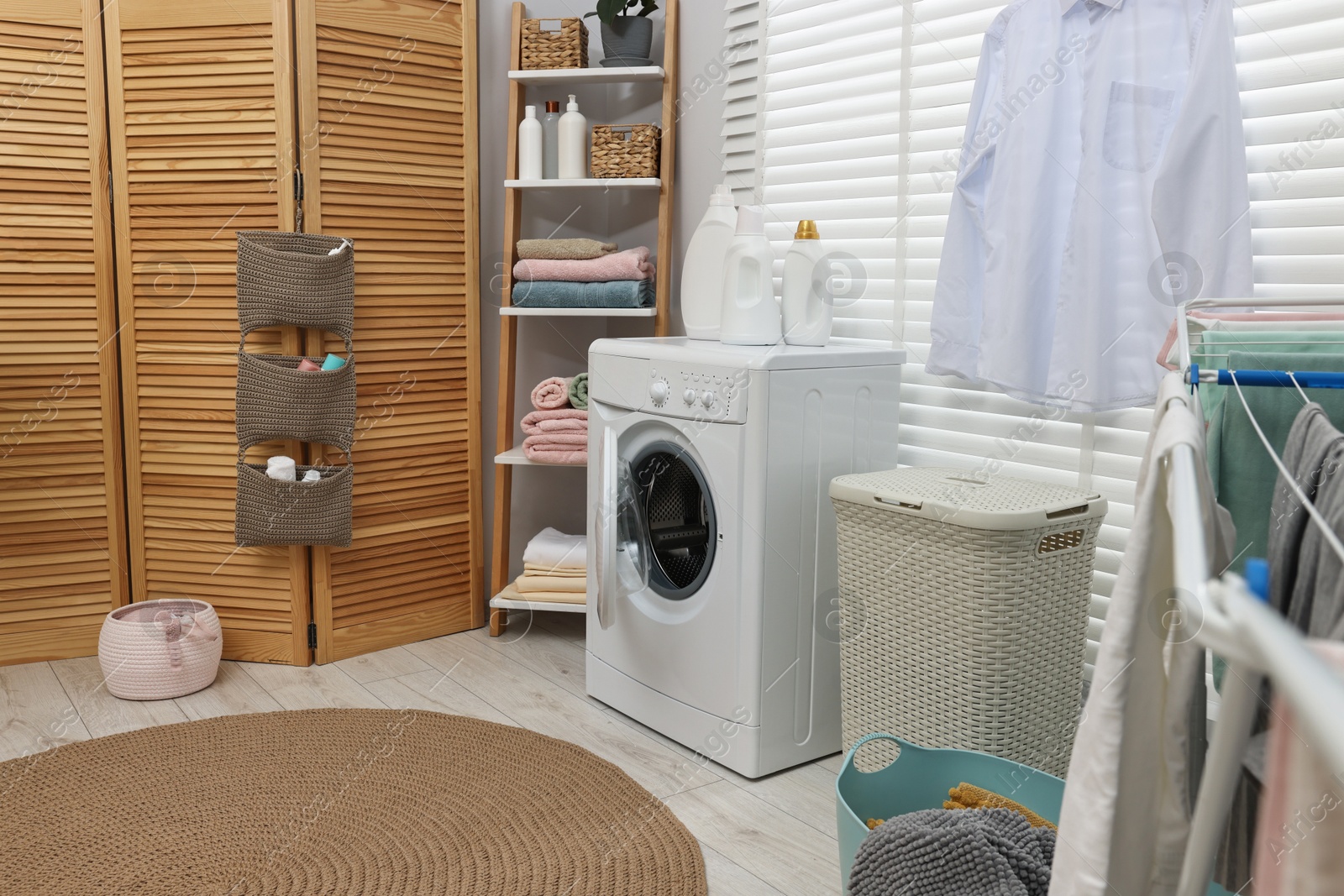 Photo of Washing machine, folding screen, detergents, towels and basket in laundry room