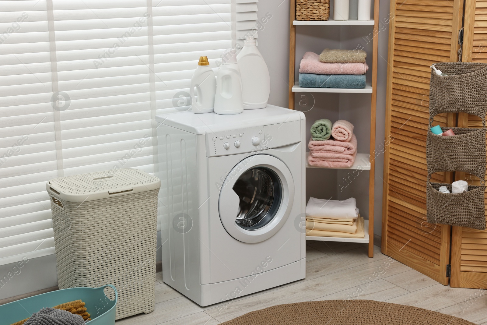 Photo of Washing machine, detergents, towels and basket in laundry room