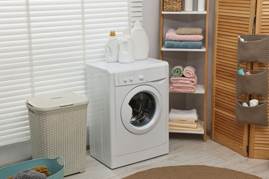 Photo of Washing machine, detergents, towels and basket in laundry room