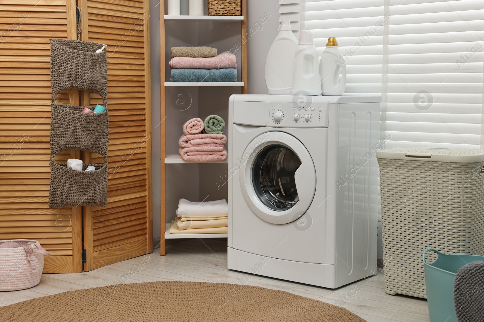 Photo of Washing machine, detergents, towels and basket in laundry room