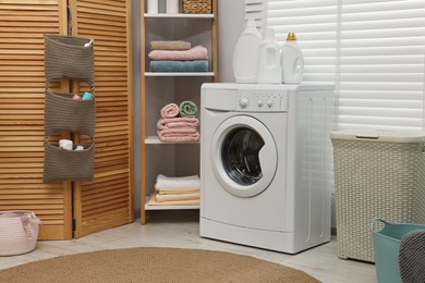 Photo of Washing machine, detergents, towels and basket in laundry room