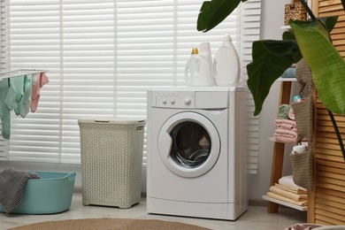 Photo of Washing machine, detergents, towels and baskets in laundry room