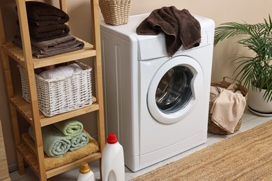 Stylish laundry room interior with washing machine, furniture, detergents and houseplant