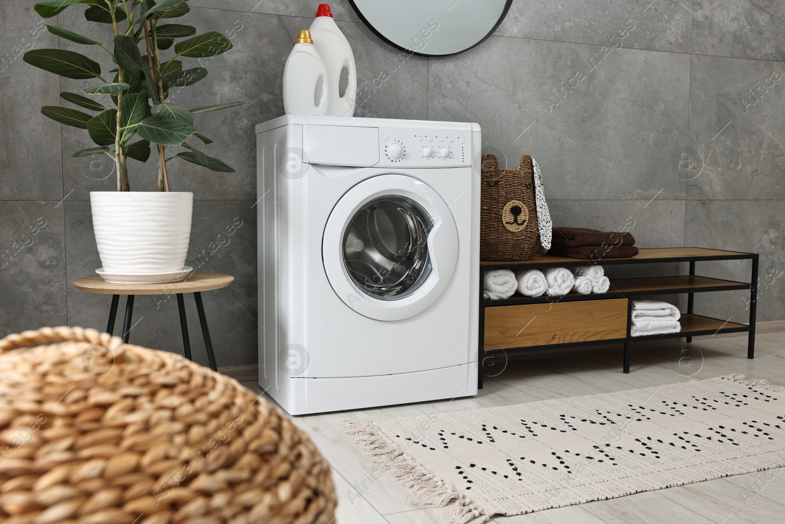 Photo of Washing machine, detergents, houseplant, baskets and storage cabinet in laundry room